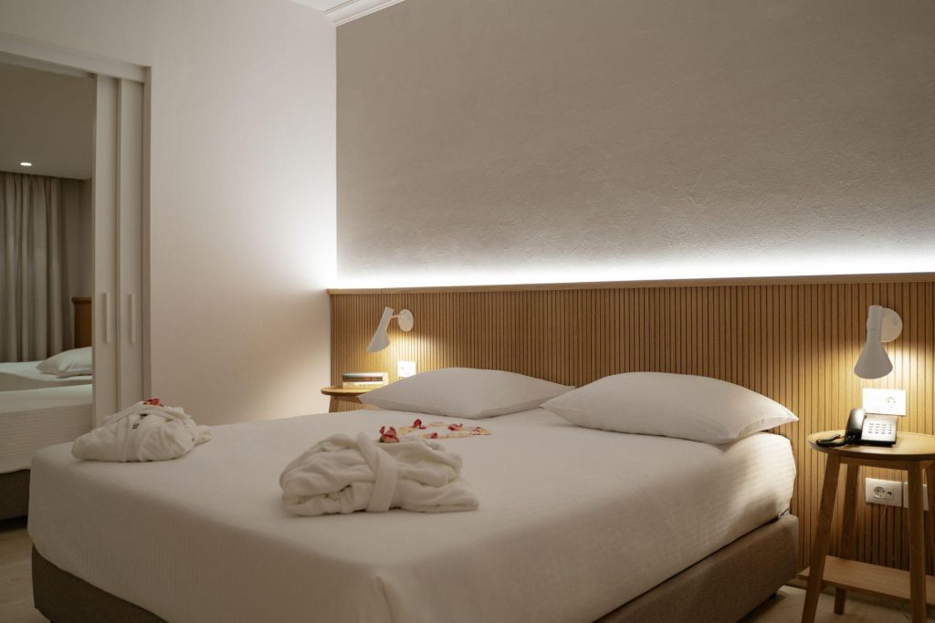 Διπλό κρεβάτι σε δωμάτιο του ξενοδοχείου Roda Beach Resort, πίσω από το οποίο υπάρχει κρυφός φωτισμός.